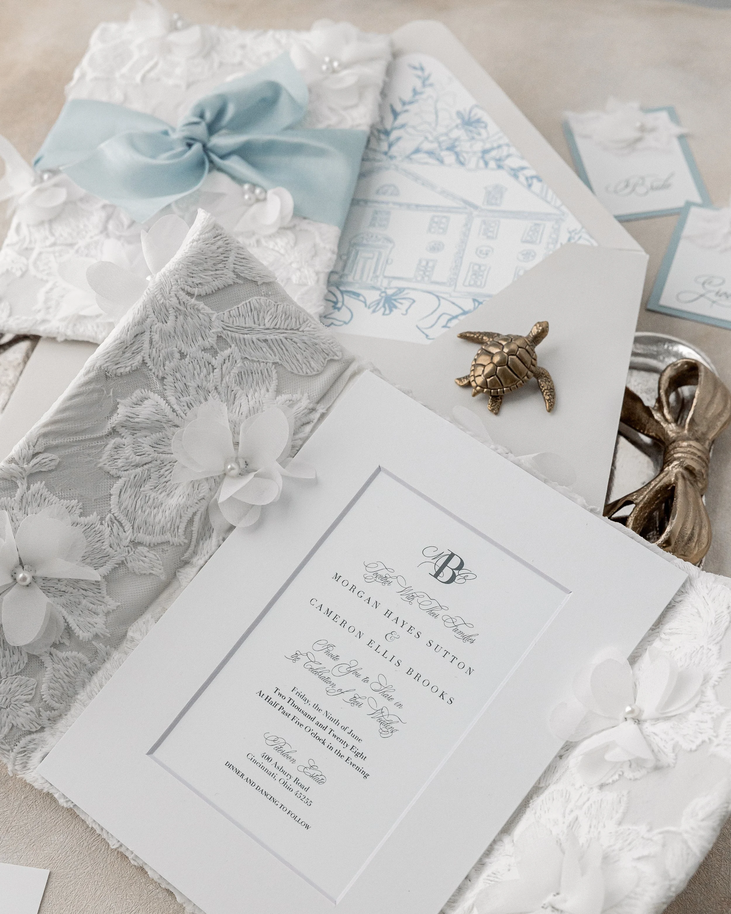 The center of the suite features a custom monogram and digitally printed type treatment beneath a white matte overlay, framed by the signature fabric detailing and dimensional pearl flowers.