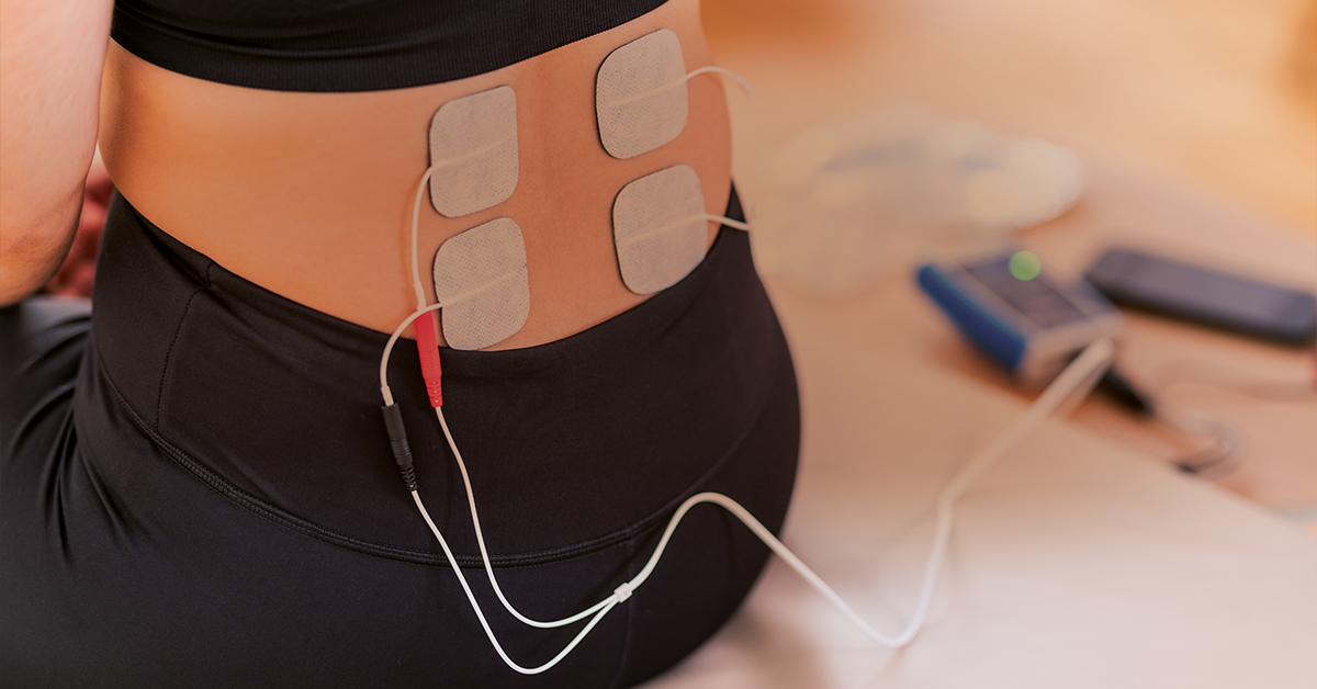 Person's abdomen with multiple electrotherapy pads attached, connected to a device for potential muscle stimulation or pain relief.