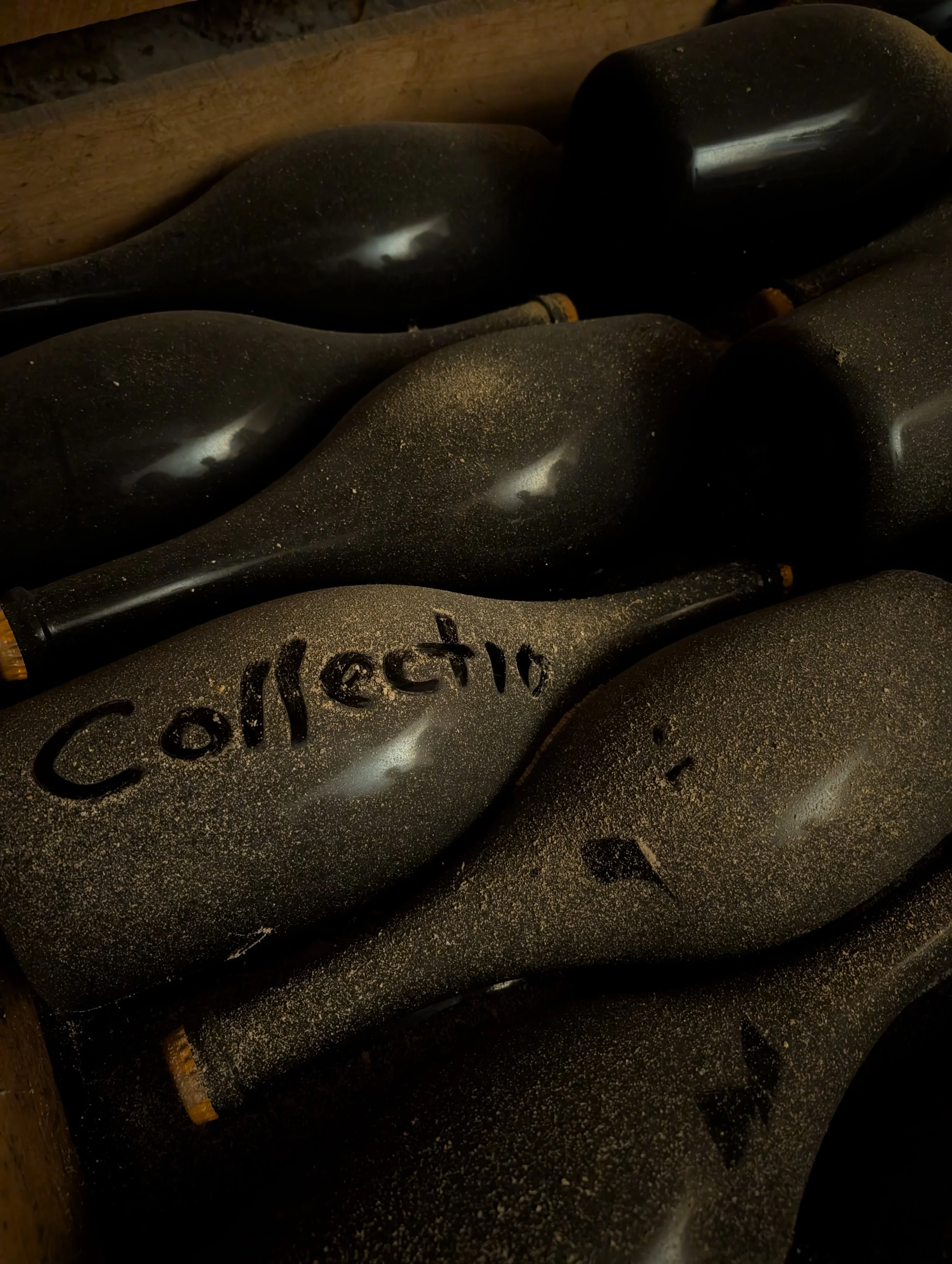 Several black wine bottles covered in gold dust with one bottle labeled 'Collective' written in black marker.