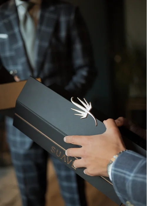 Person holding a black box with the brand name 'SUNV' and a decorative silver reindeer ornament attached, with another person in a plaid suit in the background.