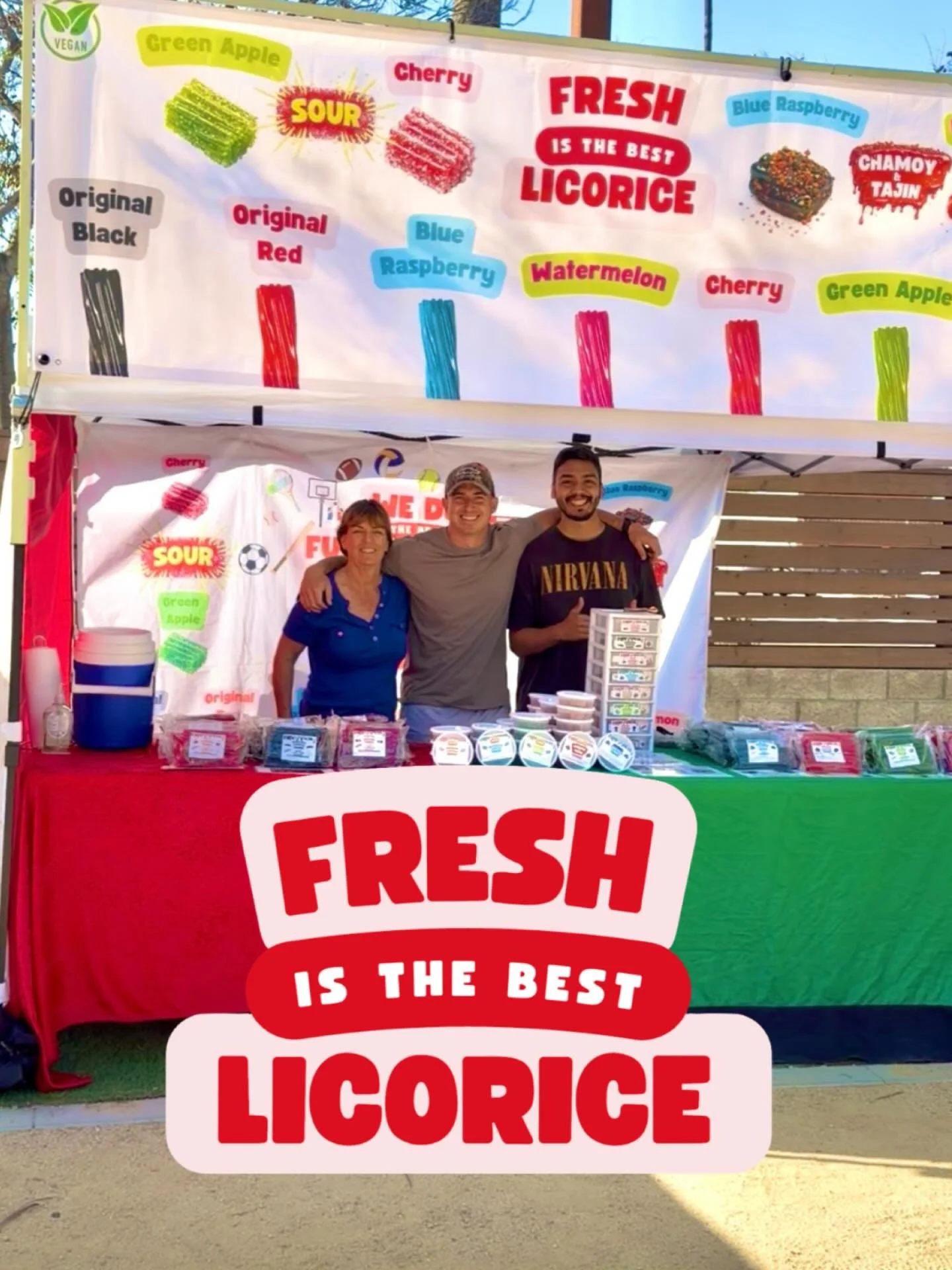 A colorful booth selling various flavored licorice, with a large sign that reads "FRESH IS THE BEST LICORICE." There are three people standing behind the booth, smiling.