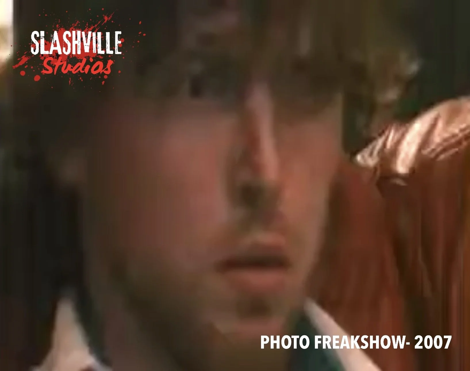 Close-up of a young man with messy hair, and an expression of surprise or concern, with a blurred background and text overlay from a 2007 photo at Slashville Studios.