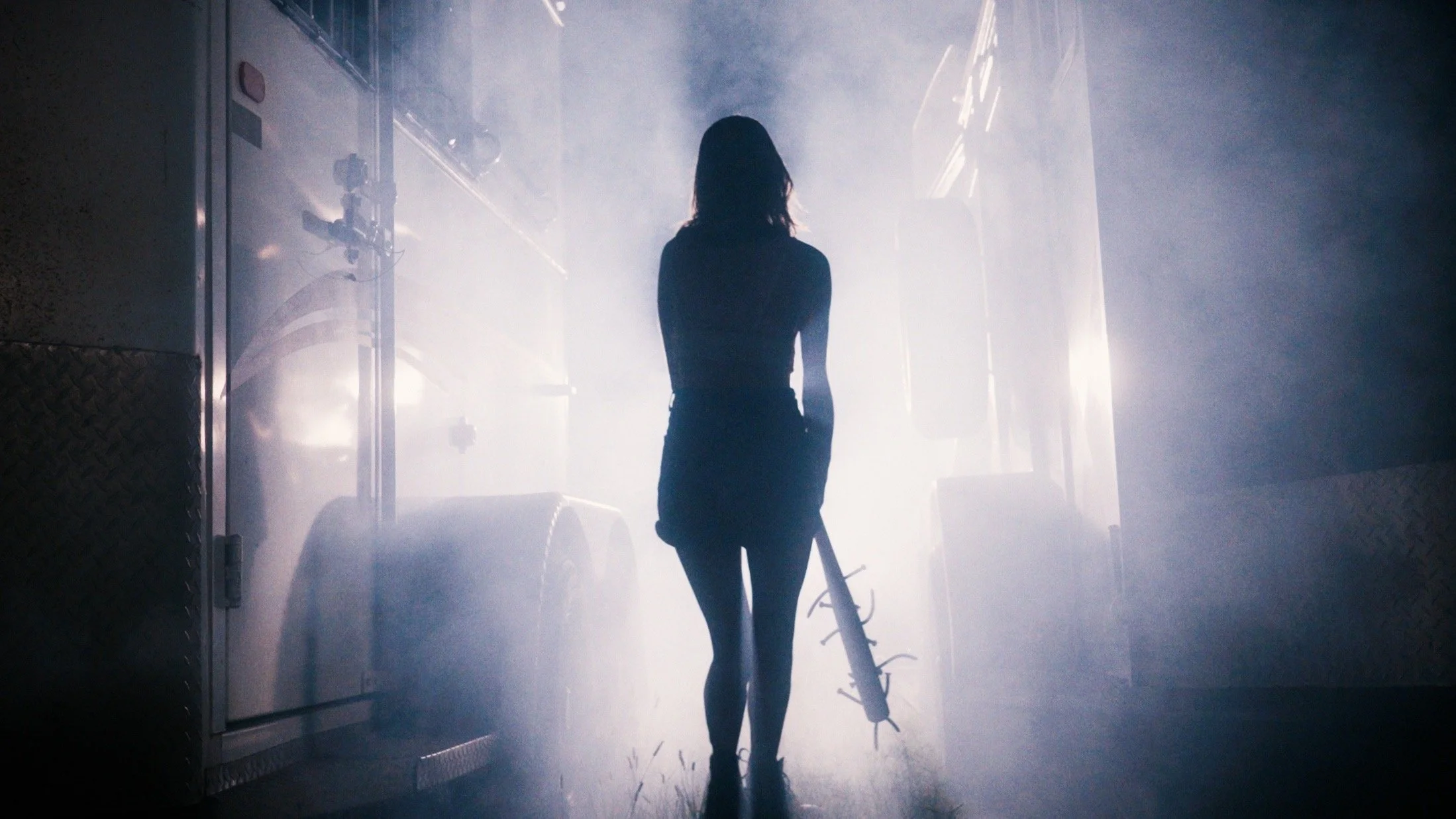 Silhouette of a woman holding a spiked baseball bat, walking towards a bright light in a smoky environment.