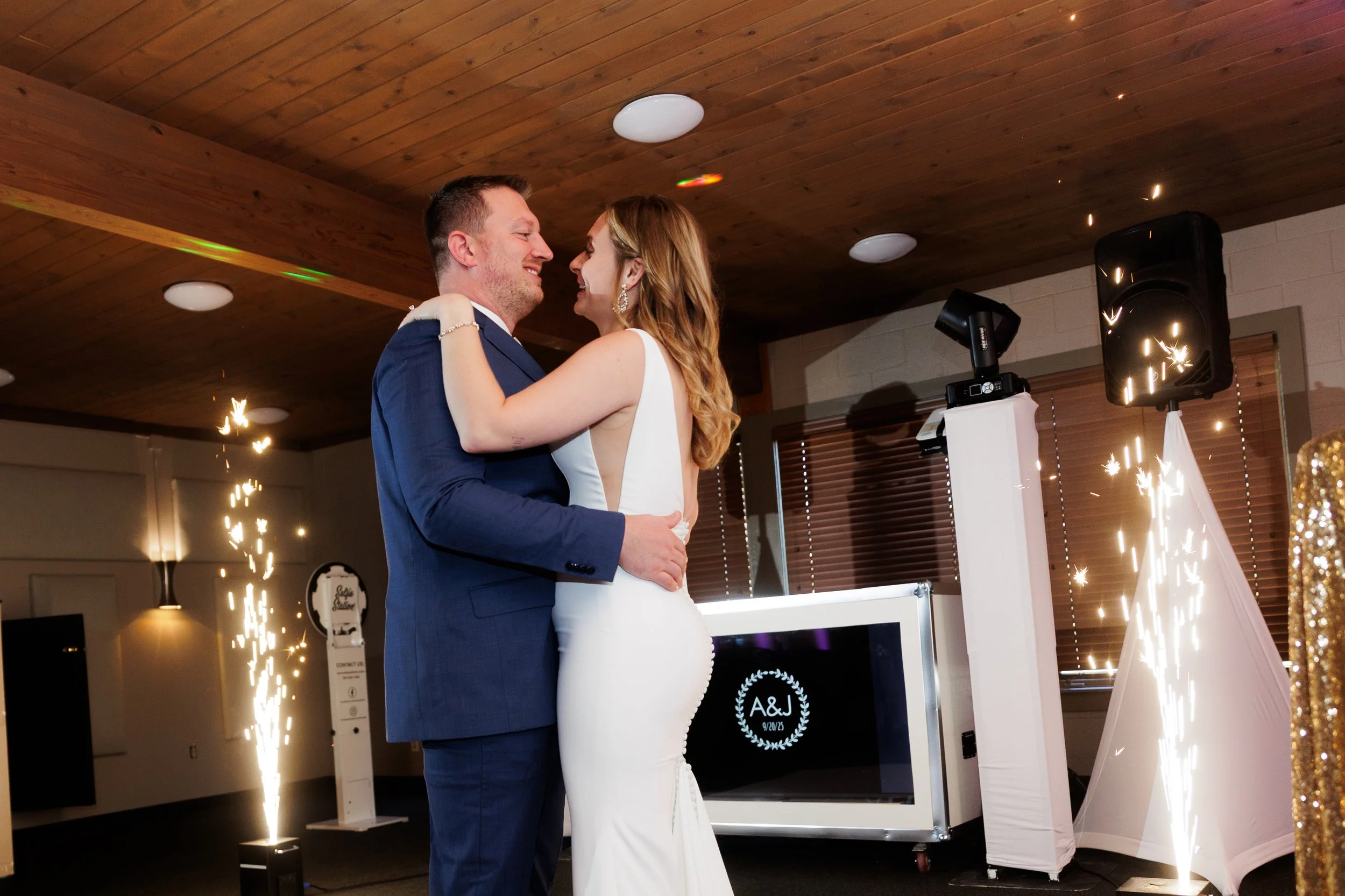 A newlywed couple dancing at their wedding reception, surrounded by sparklers and wedding decoration in a decorated indoor venue.