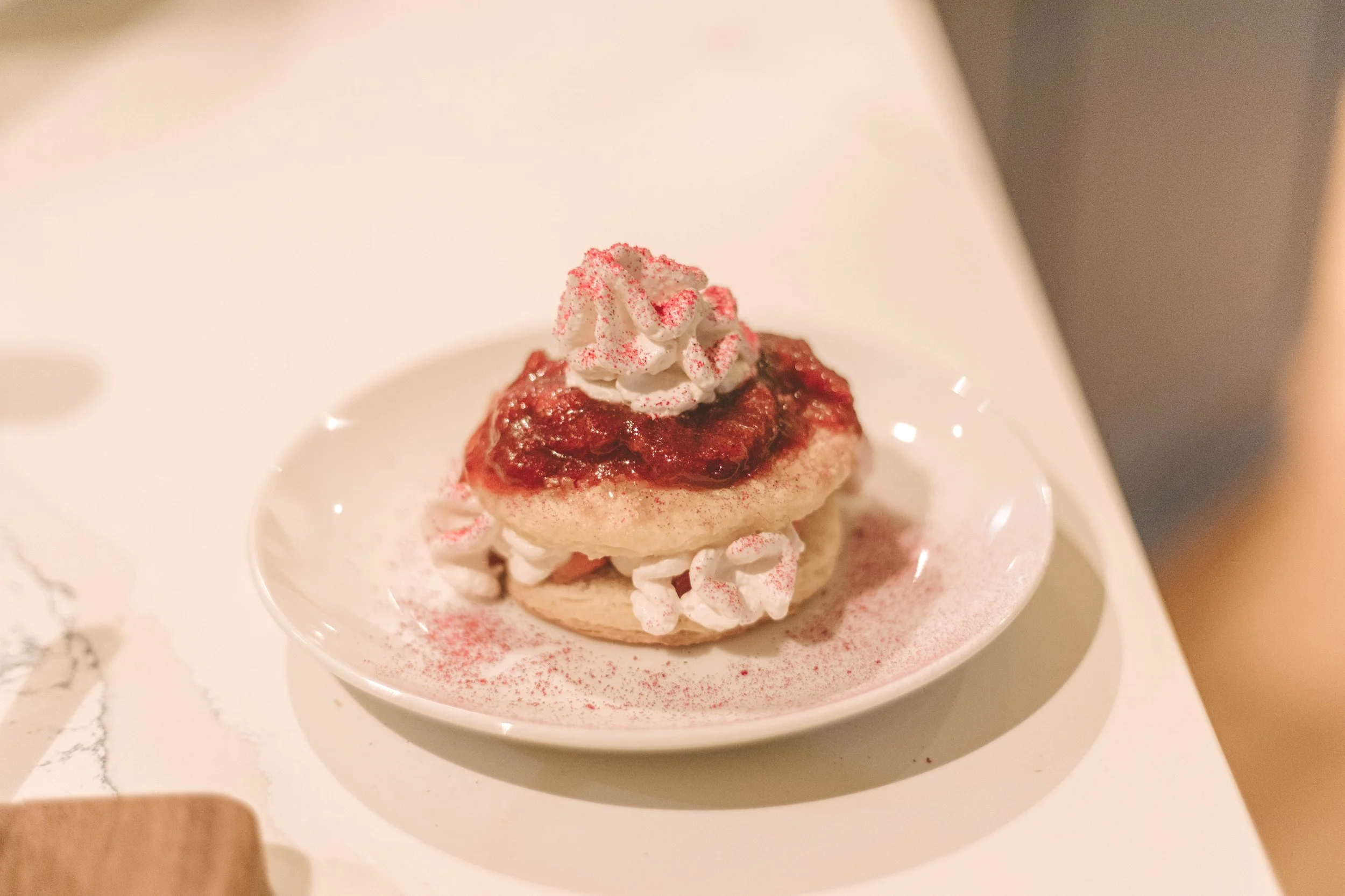 A cupcake topped with whipped cream and red sprinkles sitting in a small white bowl.