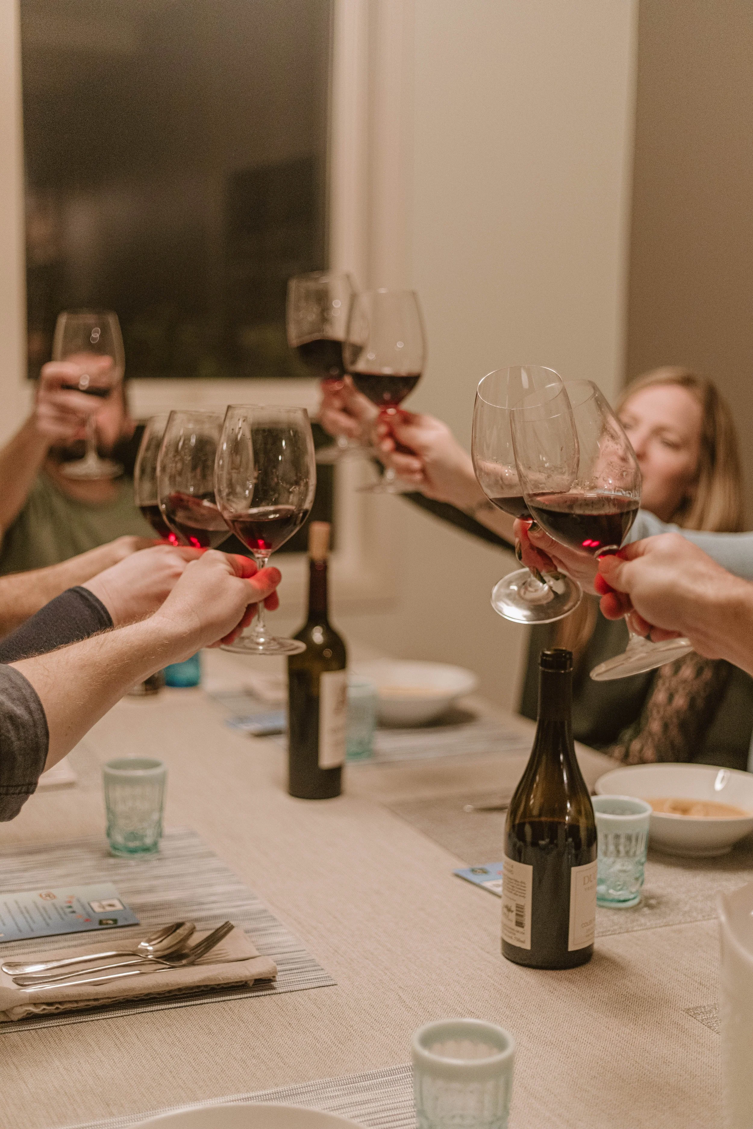 People raising glasses of red wine in a toast at a dinner party.