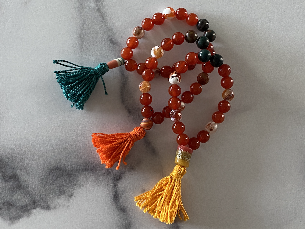 Colorful beaded prayer or meditation beads with multicolored tassels on a light surface.