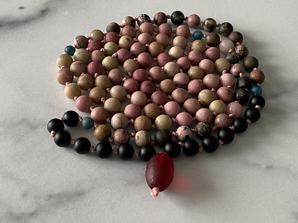 Colorful beaded necklace with a red oval pendant laid on a plain white surface.