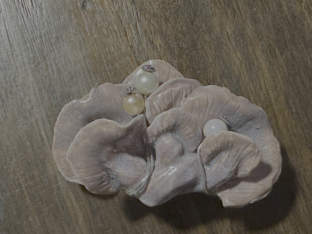 A decorative wooden surface with a leaf-shaped ceramic dish holding three pearl earrings and a small decorative pearl.
