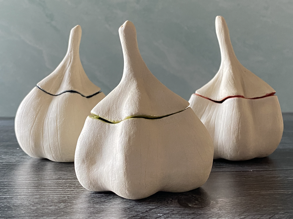 Three decorative garlic bulb sculptures with colored lines around their middle, placed on a dark wooden surface.