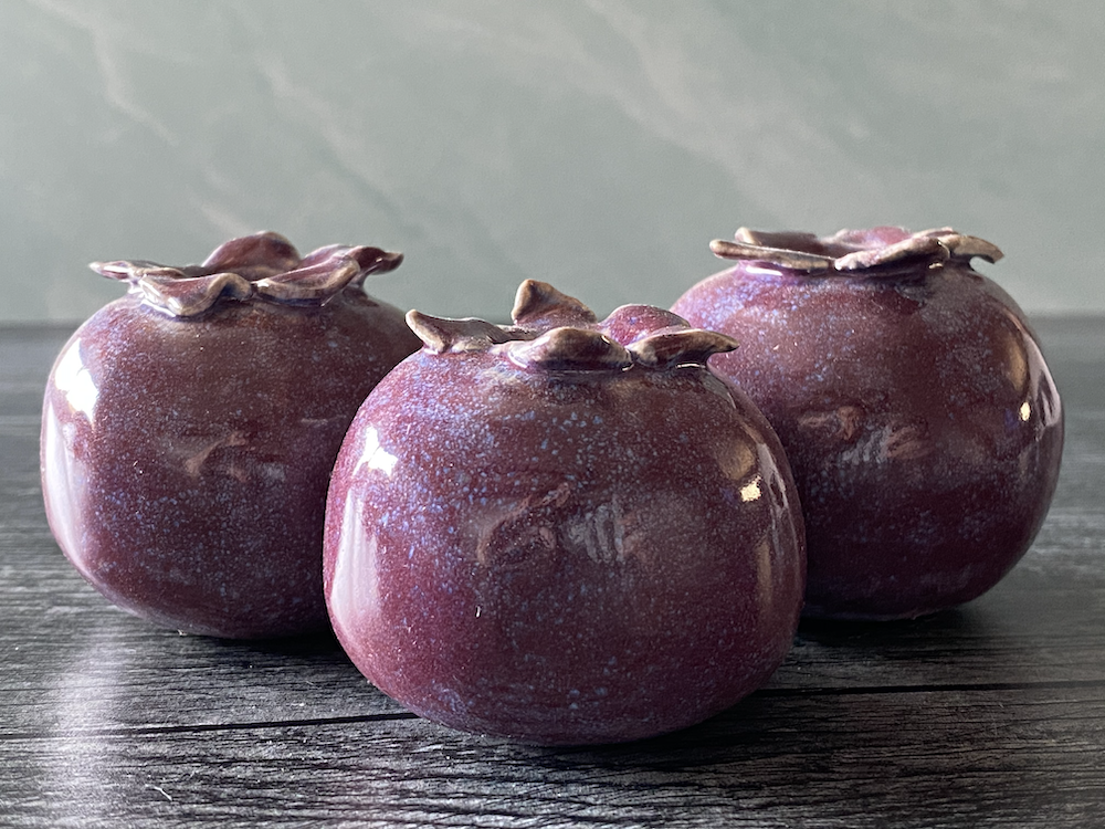 Three ceramic pomegranate-shaped vases on a dark wooden surface.