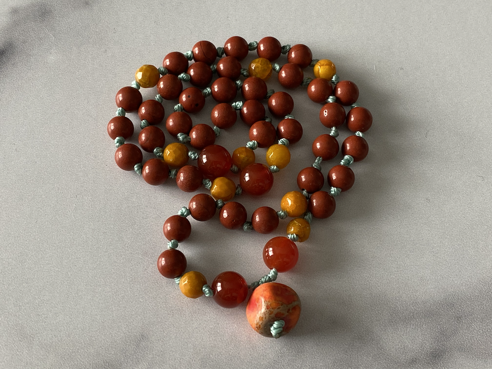 A beaded necklace with red, yellow, and marbled orange beads, arranged on a light gray surface.