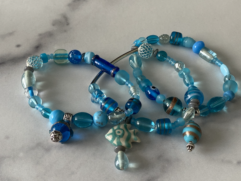 Blue beaded jewelry pieces with various shades of blue beads, some with metallic accents, and a star-shaped bead with a white and blue pattern, lying on a light surface.
