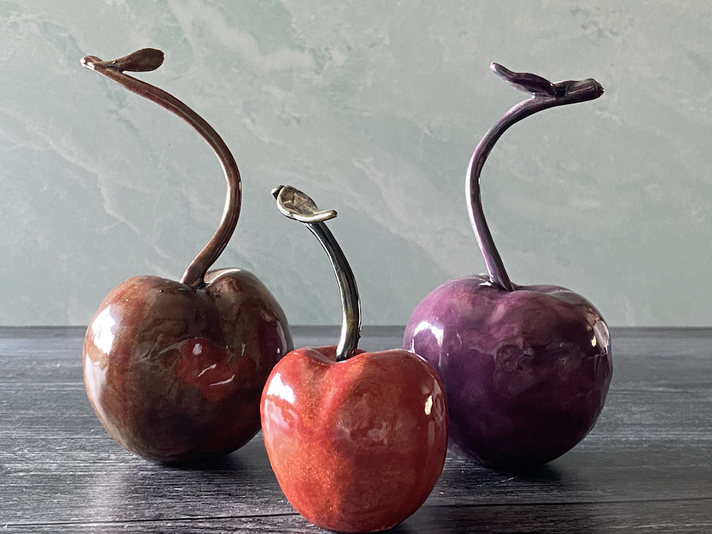 Three decorative glass cherries on a wooden surface, with a light green wall in the background.