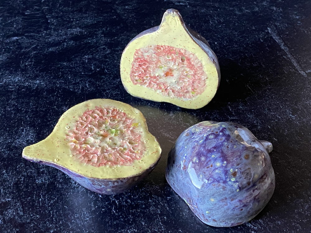 Close-up of a halved and a whole fig on a dark surface, showing the pinkish interior and purple skin.
