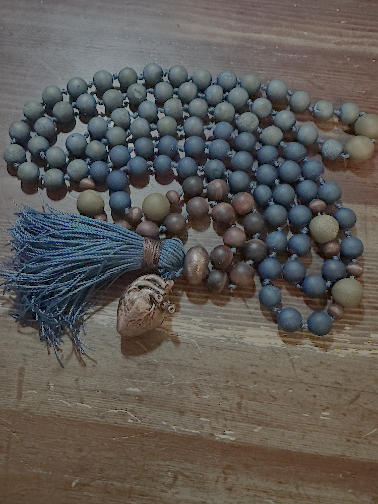 A string of blue, gray, and brown beads with a blue tassel and a seashell on a wooden surface.
