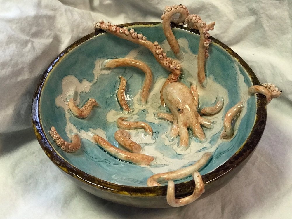 Ceramic bowl with a blue interior and dark rim containing ceramic octopus tentacles.