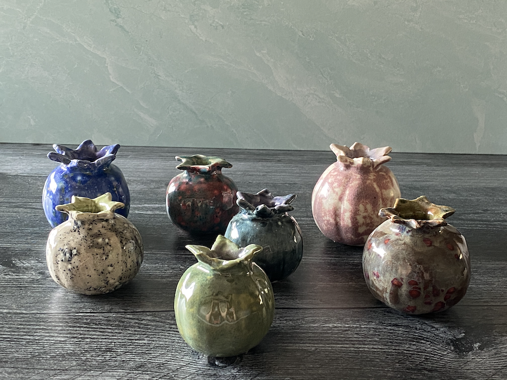 Seven small, colorful ceramic vases with ruffled mouths on a dark wooden surface, against a plain green wall.