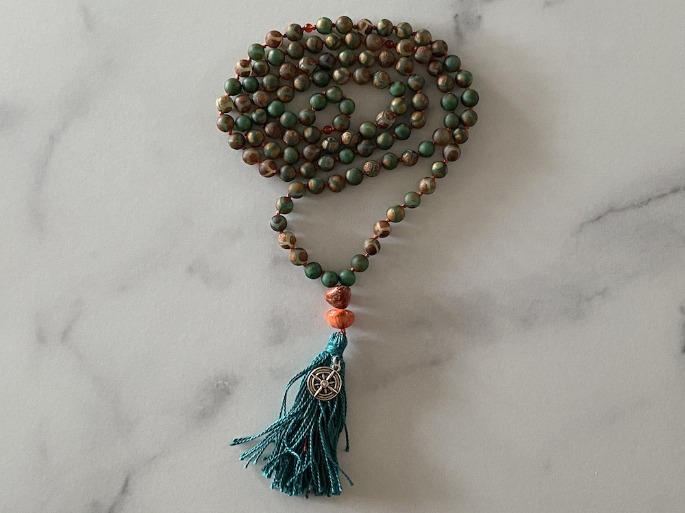 A beaded prayer necklace with a blue tassel and a metallic charm laid on a marble surface.