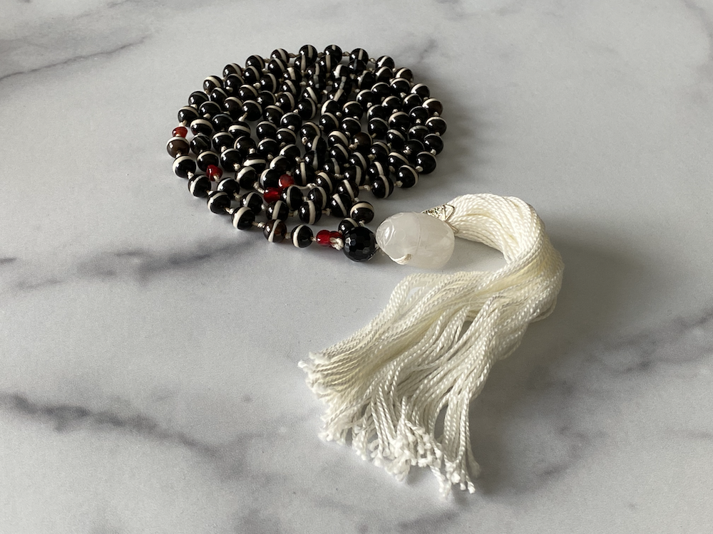 Black and white prayer beads with red accents and a white tassel resting on a marble surface.