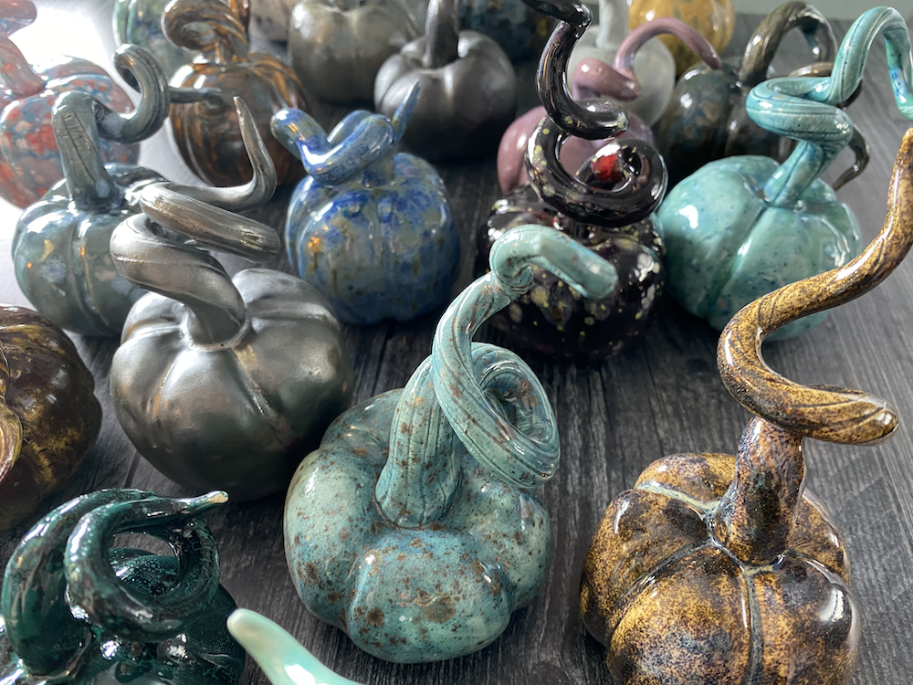 Colorful glass pumpkins with spiraled stems displayed on a wooden surface.