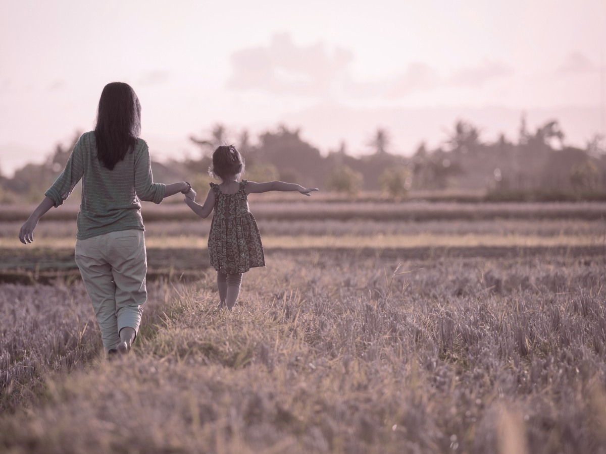 A woman and a girl holding hands walking through a lavender field at sunset.
