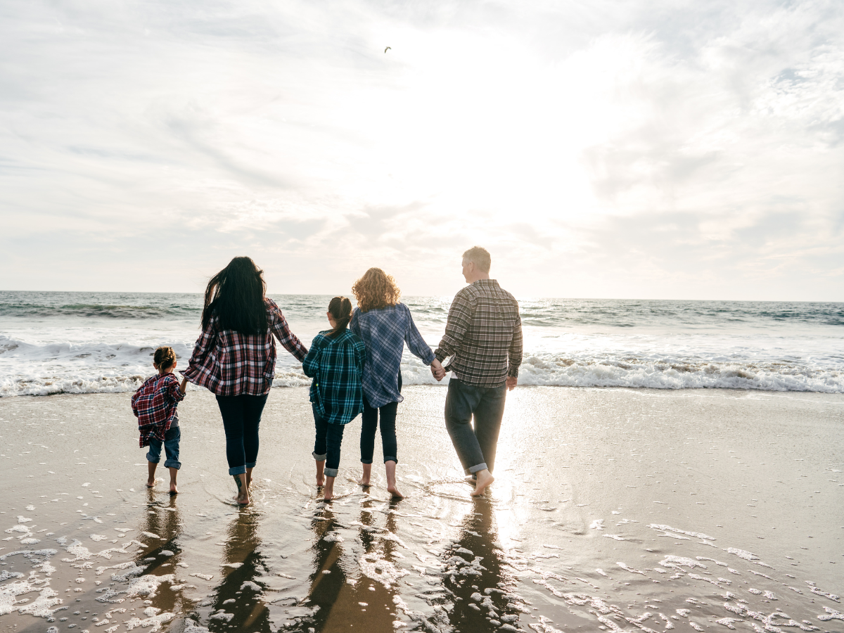 Family walking hand-in-hand on a beach at sunset.