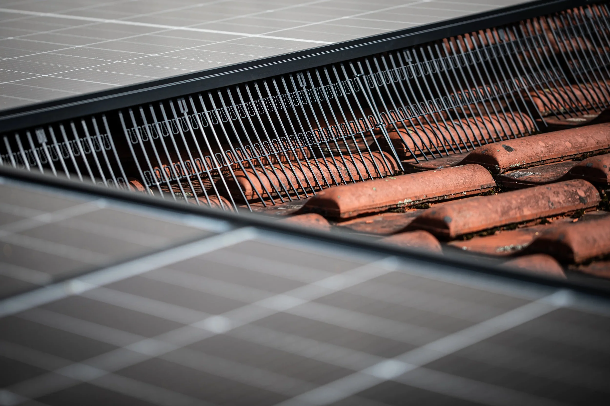 Close-up of solar panels installed on a rooftop with roof tiles visible beneath.