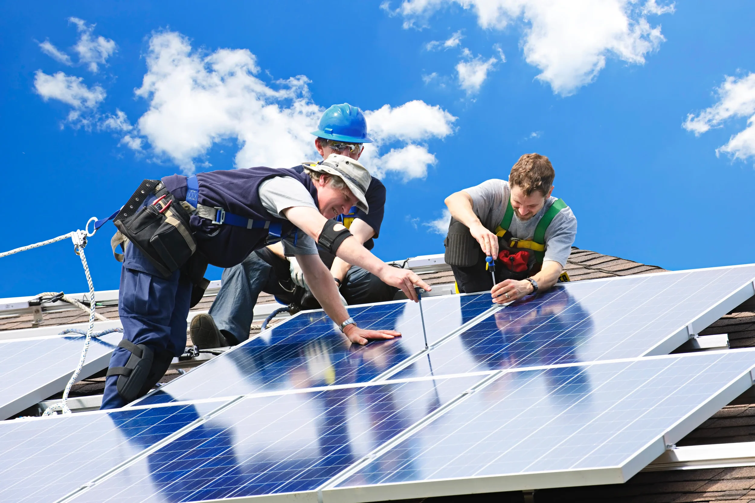 Three workers installing solar panels on a roof against a blue sky.