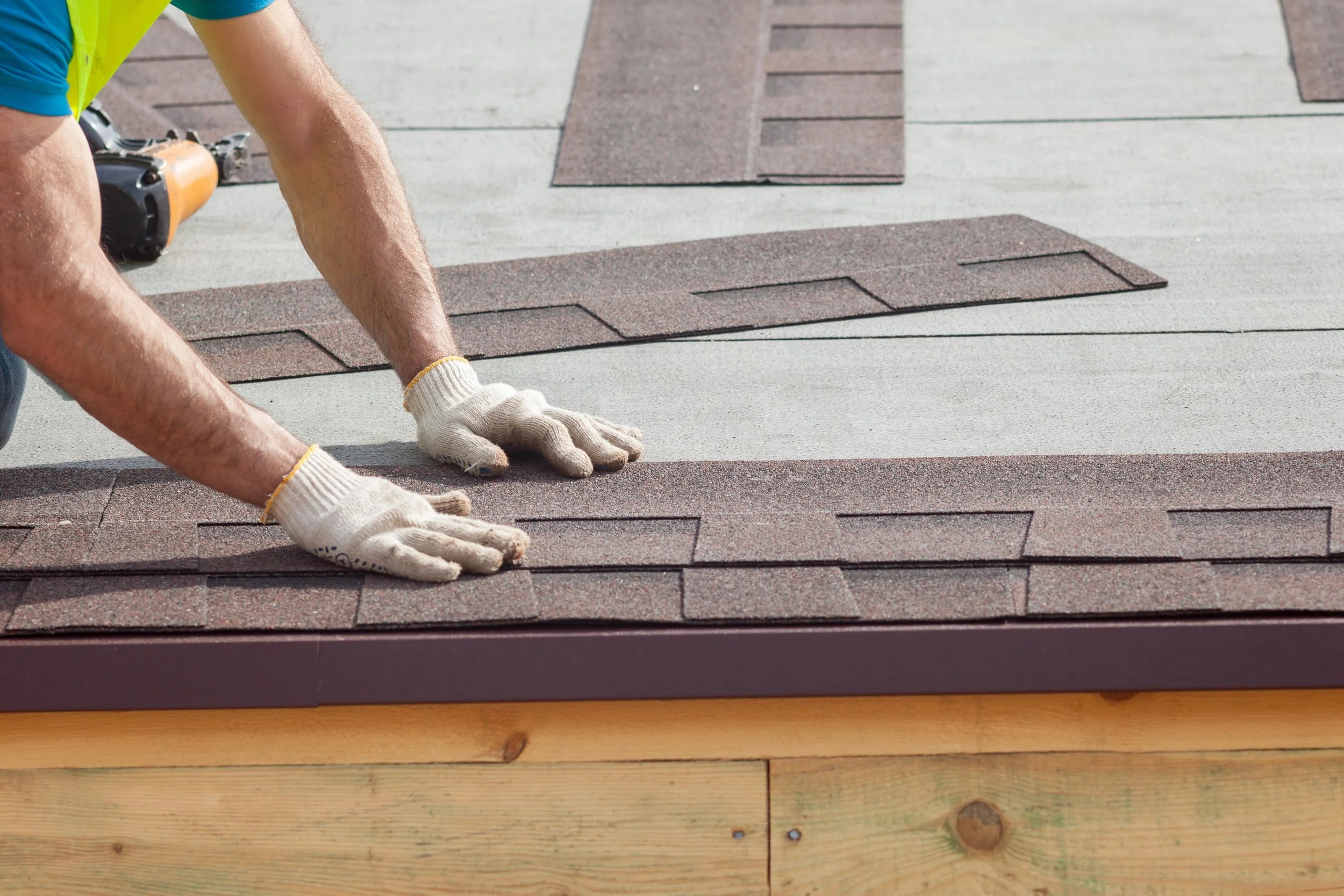 A person laying tiles on a roof, wearing gloves and a yellow safety vest, with tools nearby.