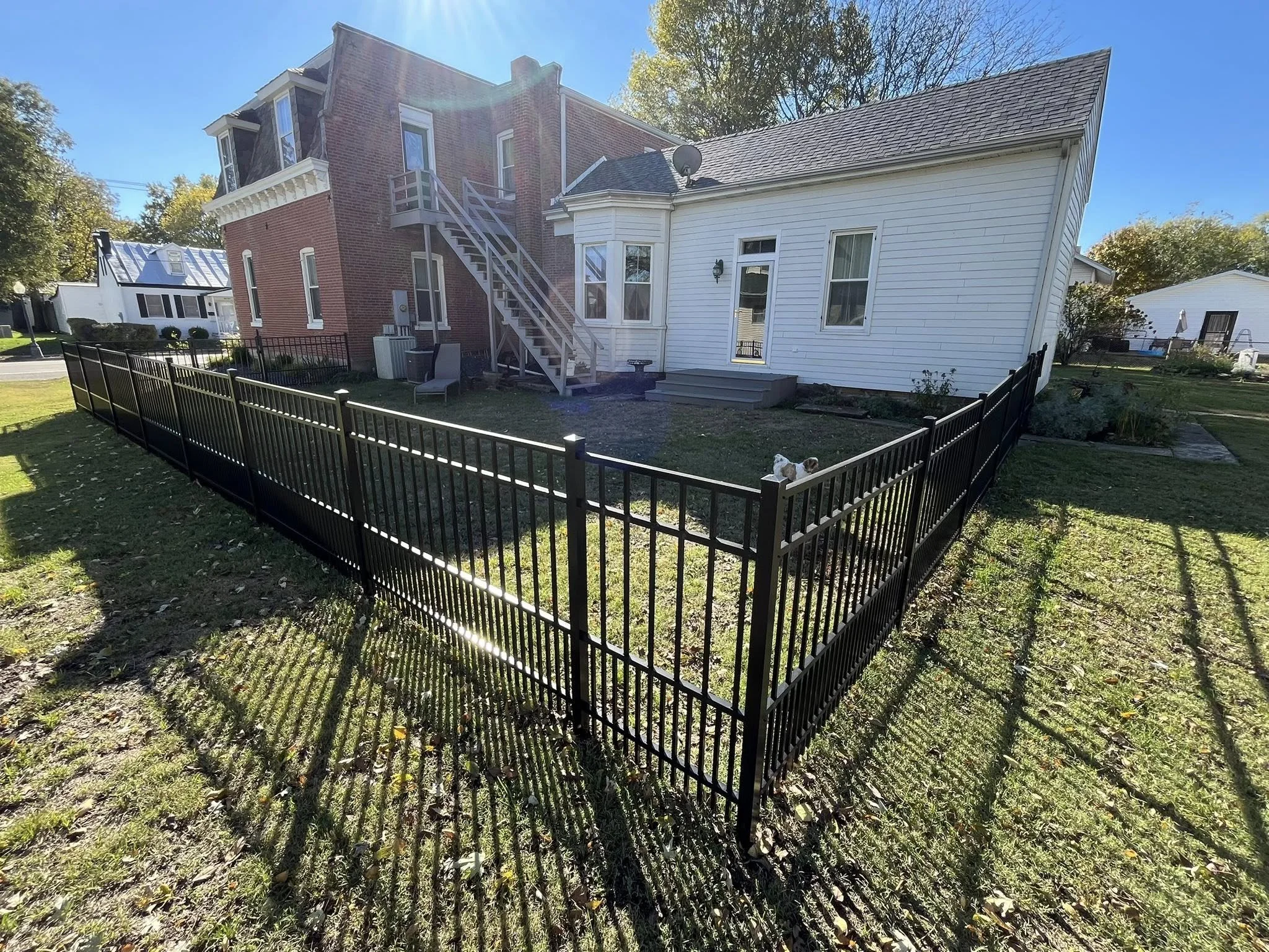 black ornamental aluminum fence in backyard around a red and a white house