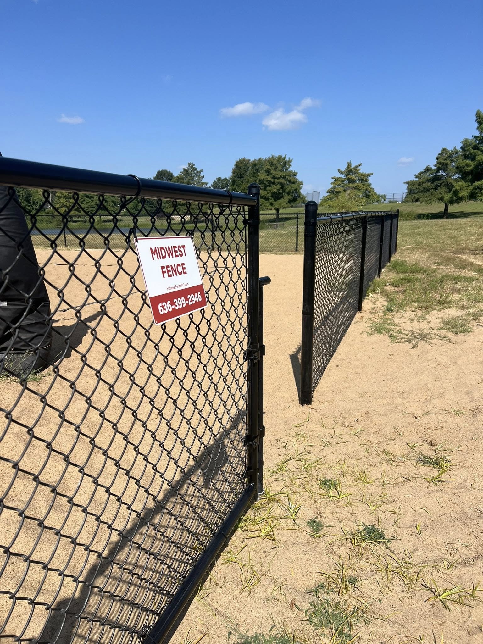 black chain link fence around sand volleyball courts at Lindenwood University with Midwest Fence sign