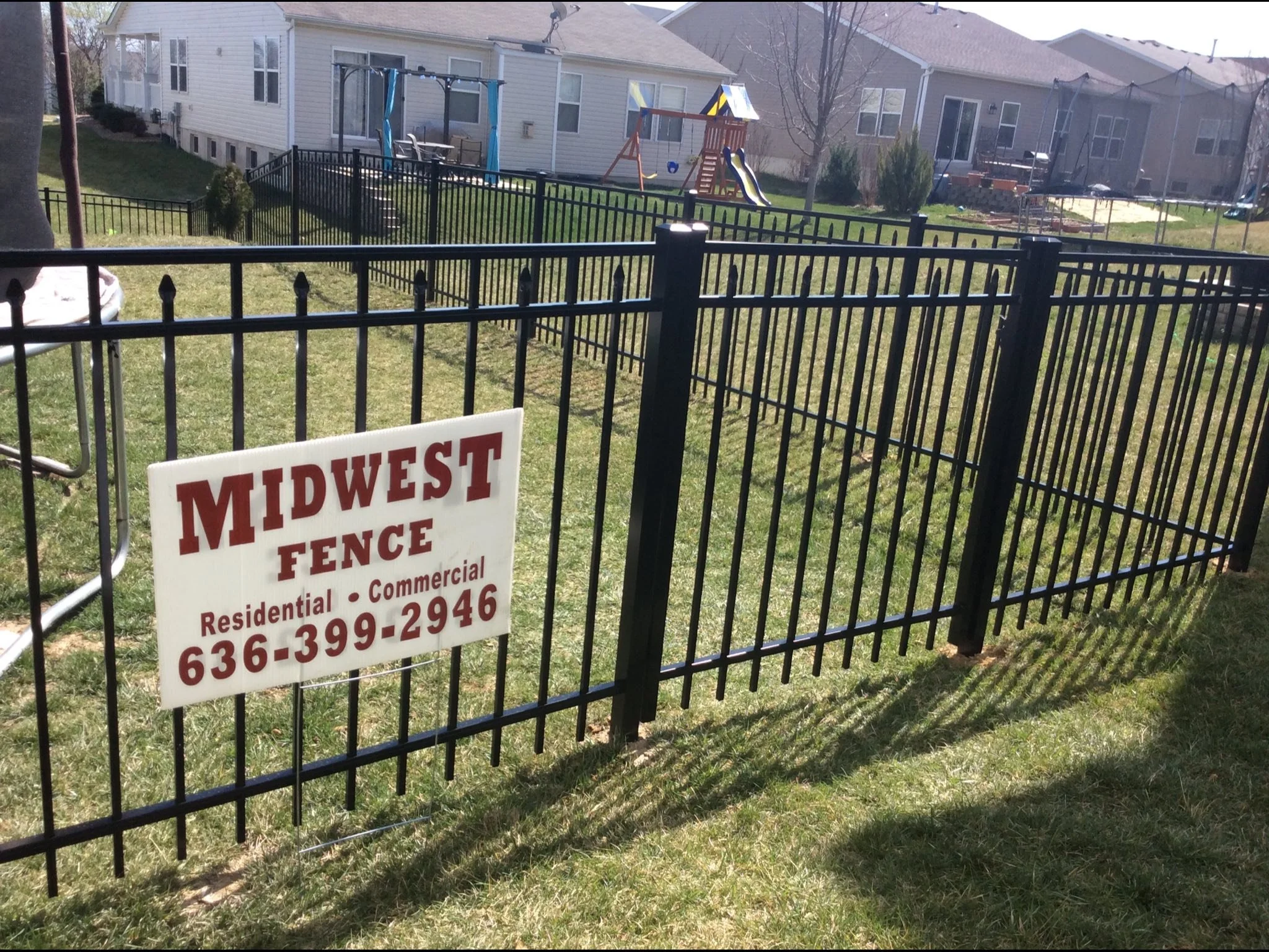 black ornamental aluminum fence in backyard with Midwest Fence sign in front