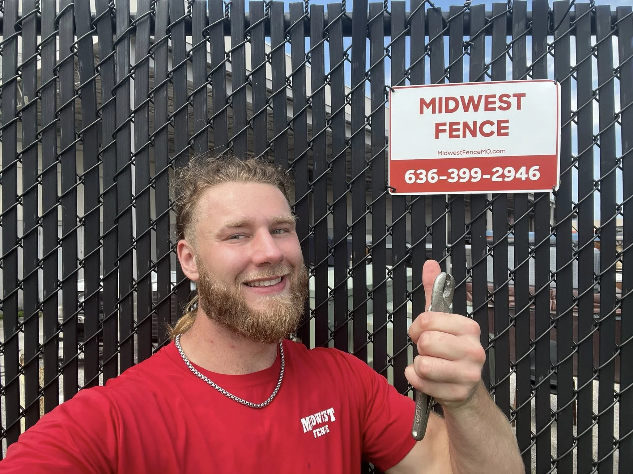 Midwest fence employee in front of black chain link privacy fence and Midwest Fence sign
