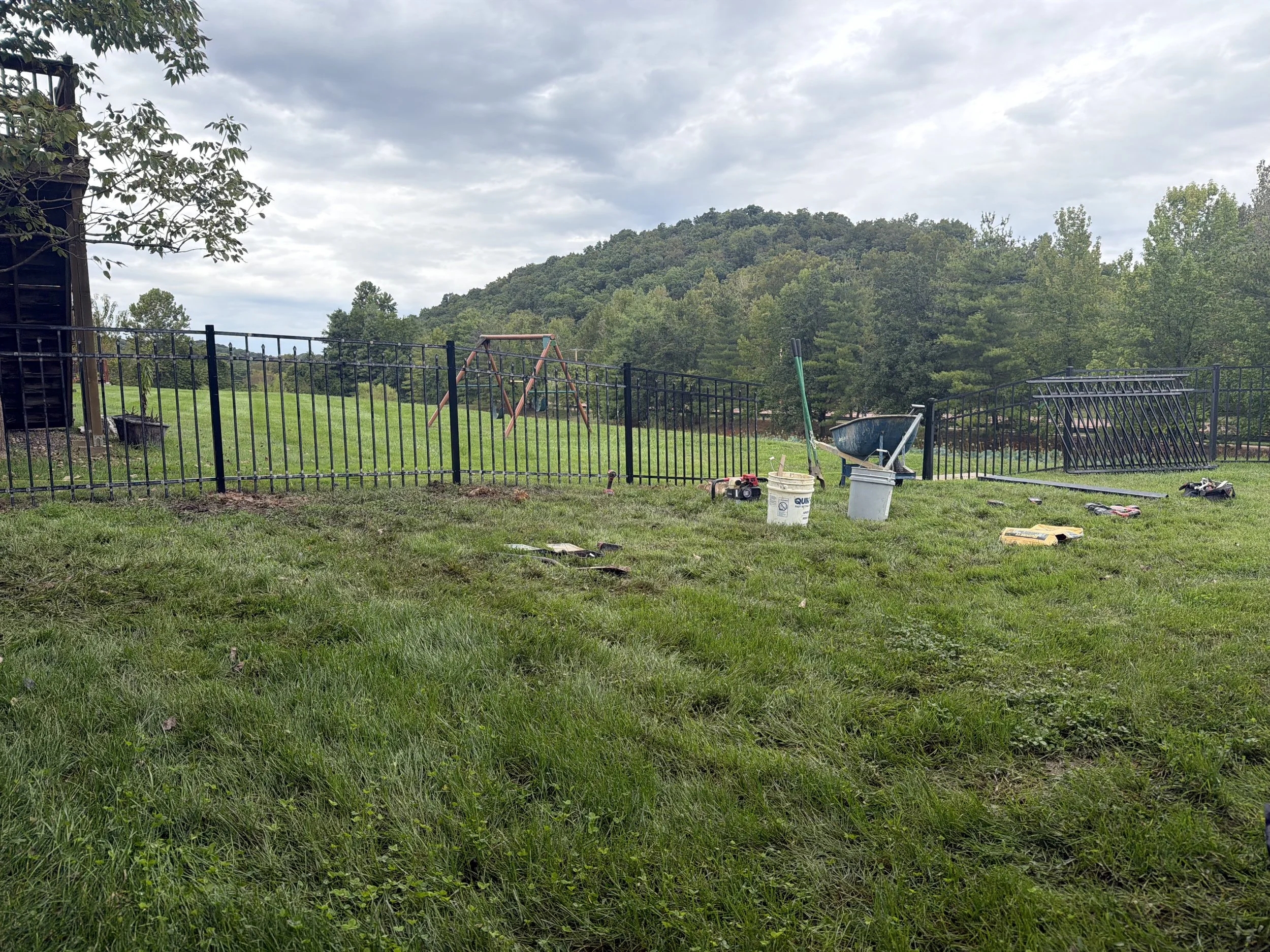 Black ornamental aluminum fence following the slope of a grassy St. Charles yard with trees beyond it.
