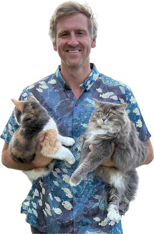 A smiling man holding two large cats, one calico and one long-haired gray.