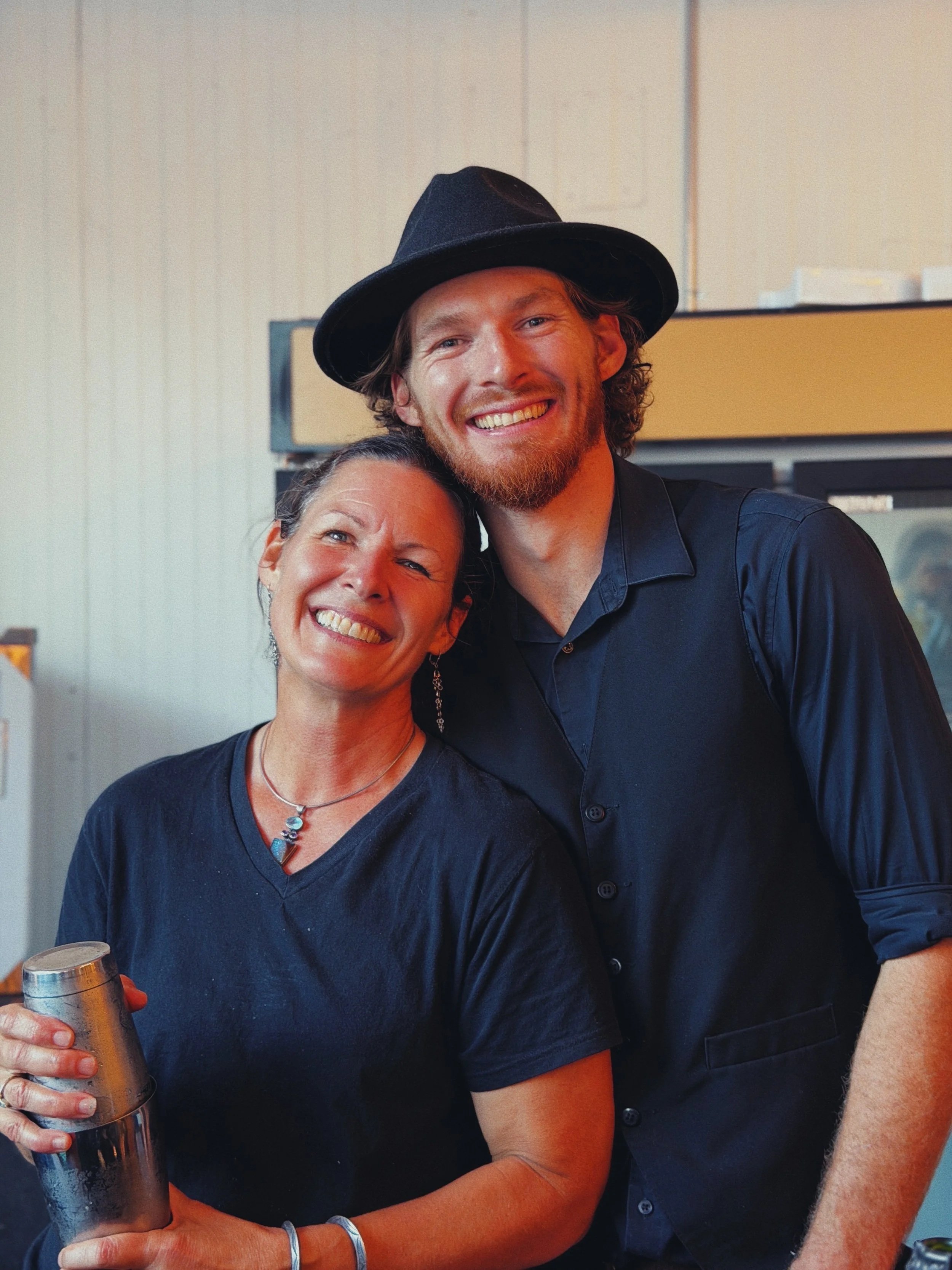 Two people smiling, one holding a metal cup, in an indoor setting.