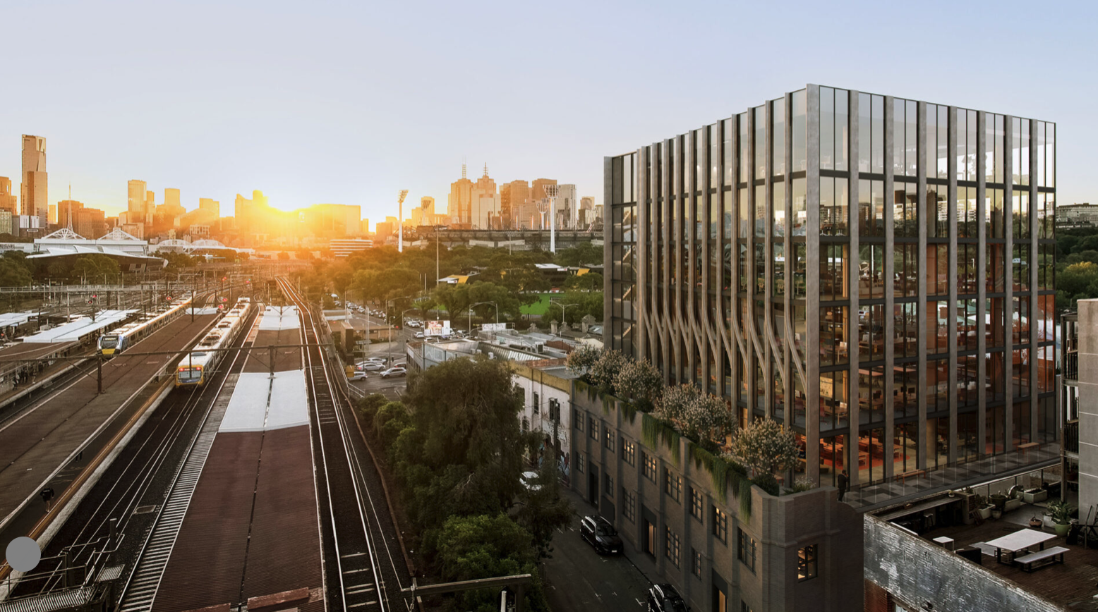 A cityscape at sunset with train tracks, trains, and high-rise buildings, including a modern glass building with outdoor greenery.
