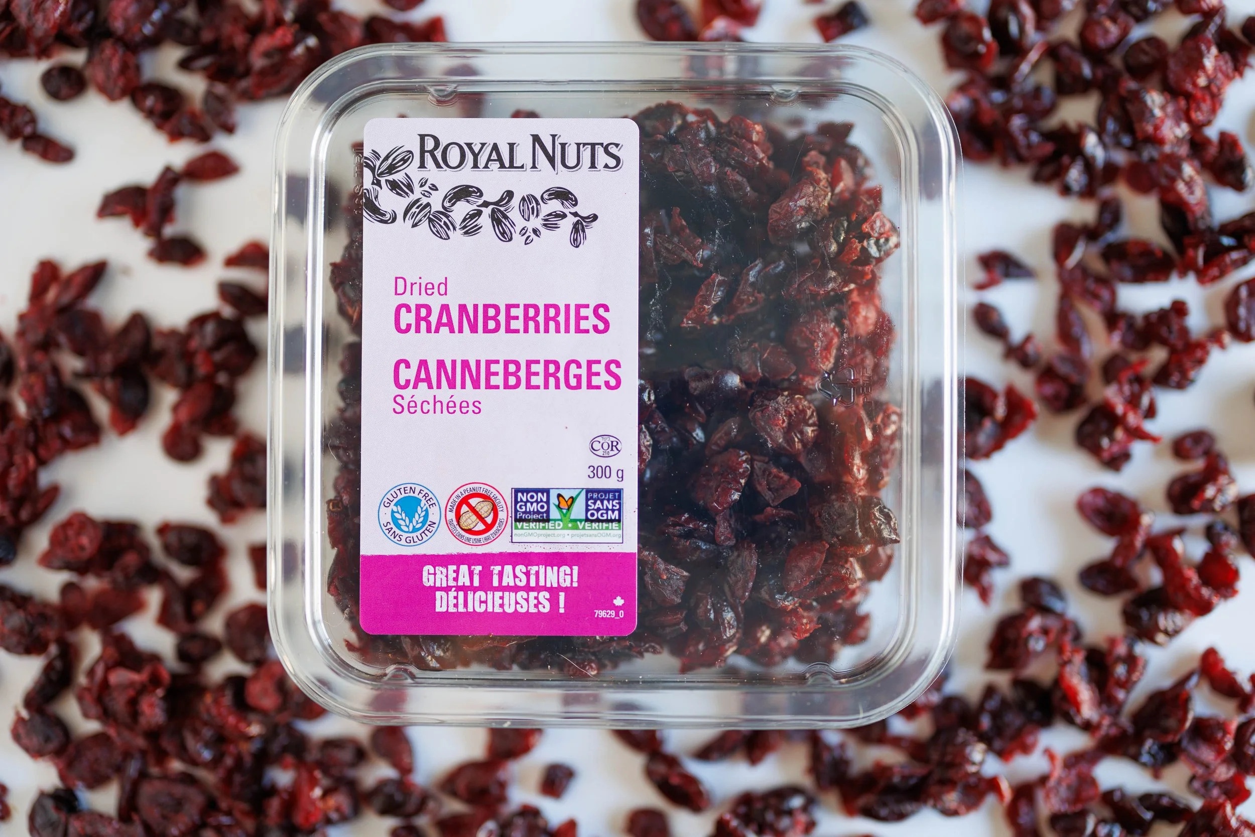 Close-up of dried apricots in a clear plastic container with a label, and some apricots on a newspaper underneath.