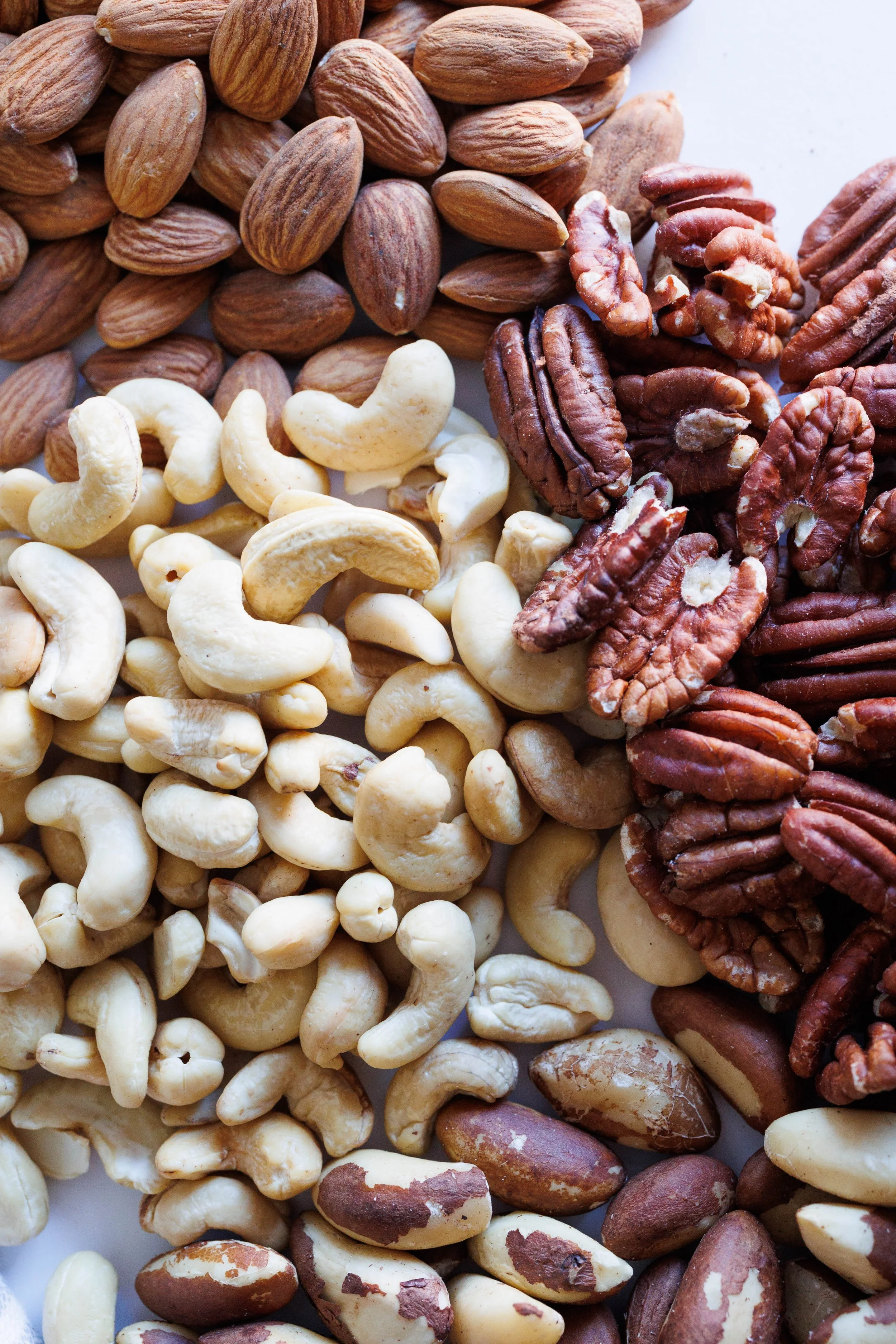 Close-up photo of mixed raw nuts including almonds, cashews, pecans, and Brazil nuts.