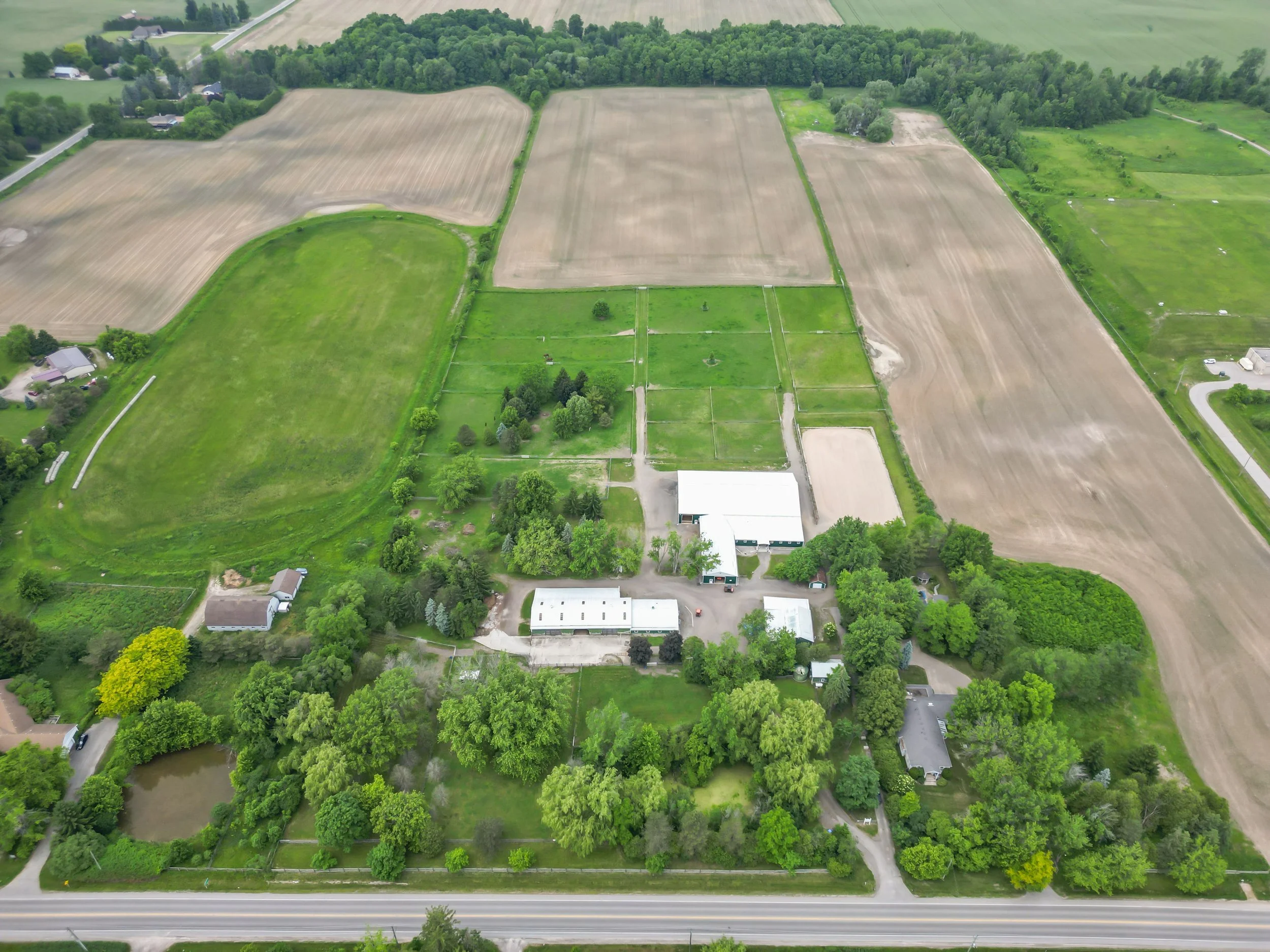 Aerial view of a rural farm with buildings, green fields, trees, and neighboring farmland.