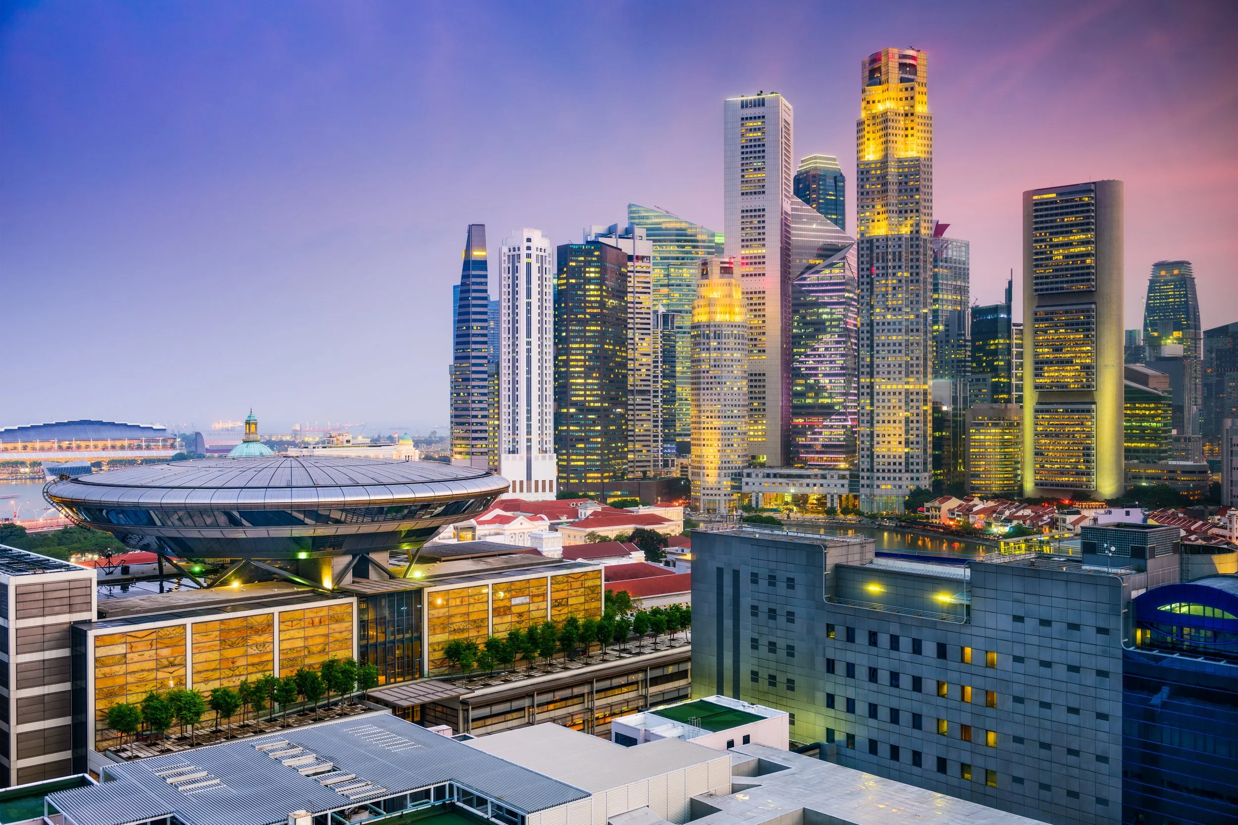 Night view of a modern city skyline with illuminated skyscrapers and a distinctive round building in the foreground.