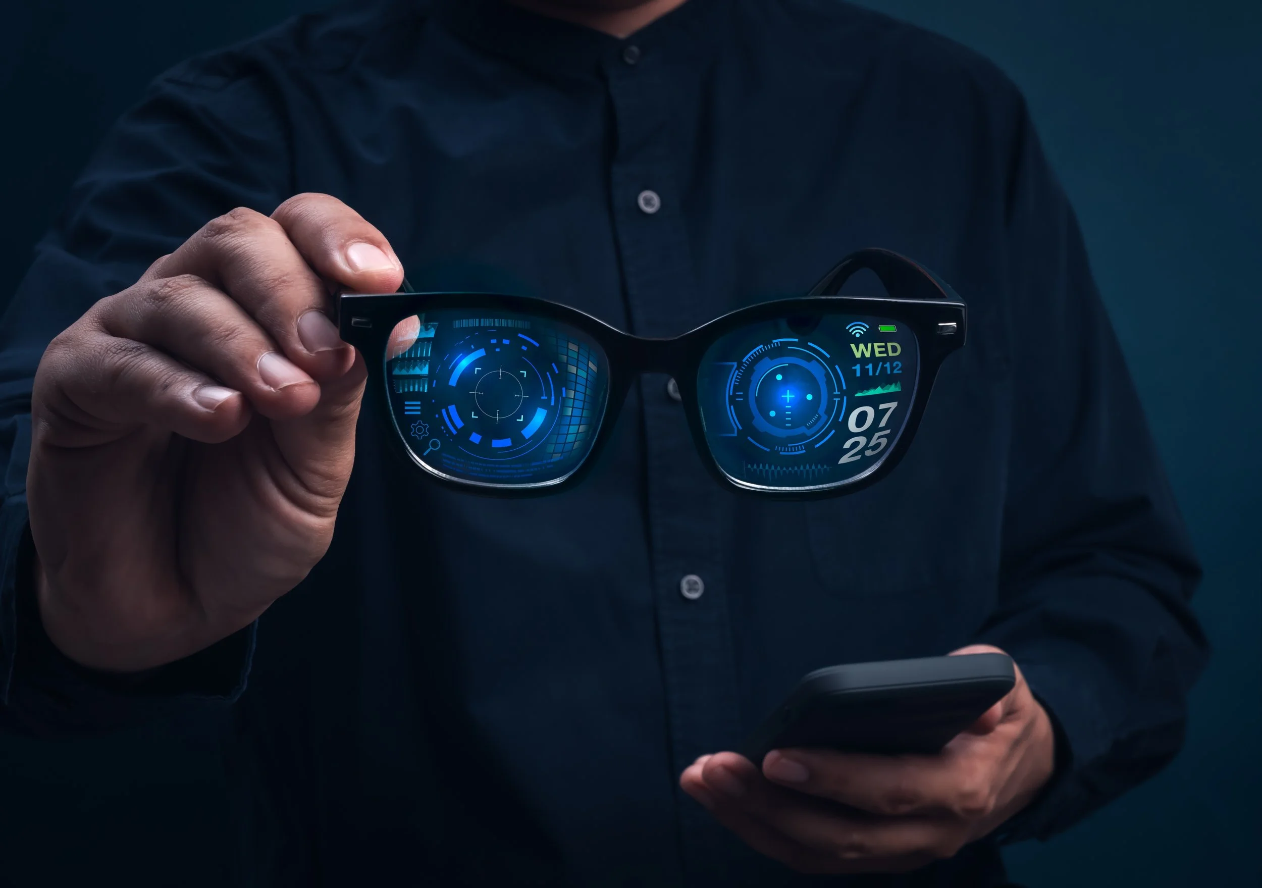 Person holding smart glasses with digital display, wearing a dark button-up shirt.