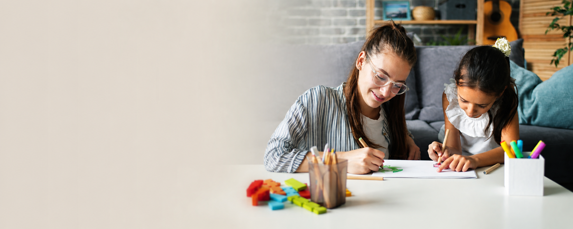 Two girls drawing and coloring at a desk with colored markers and foam shapes.