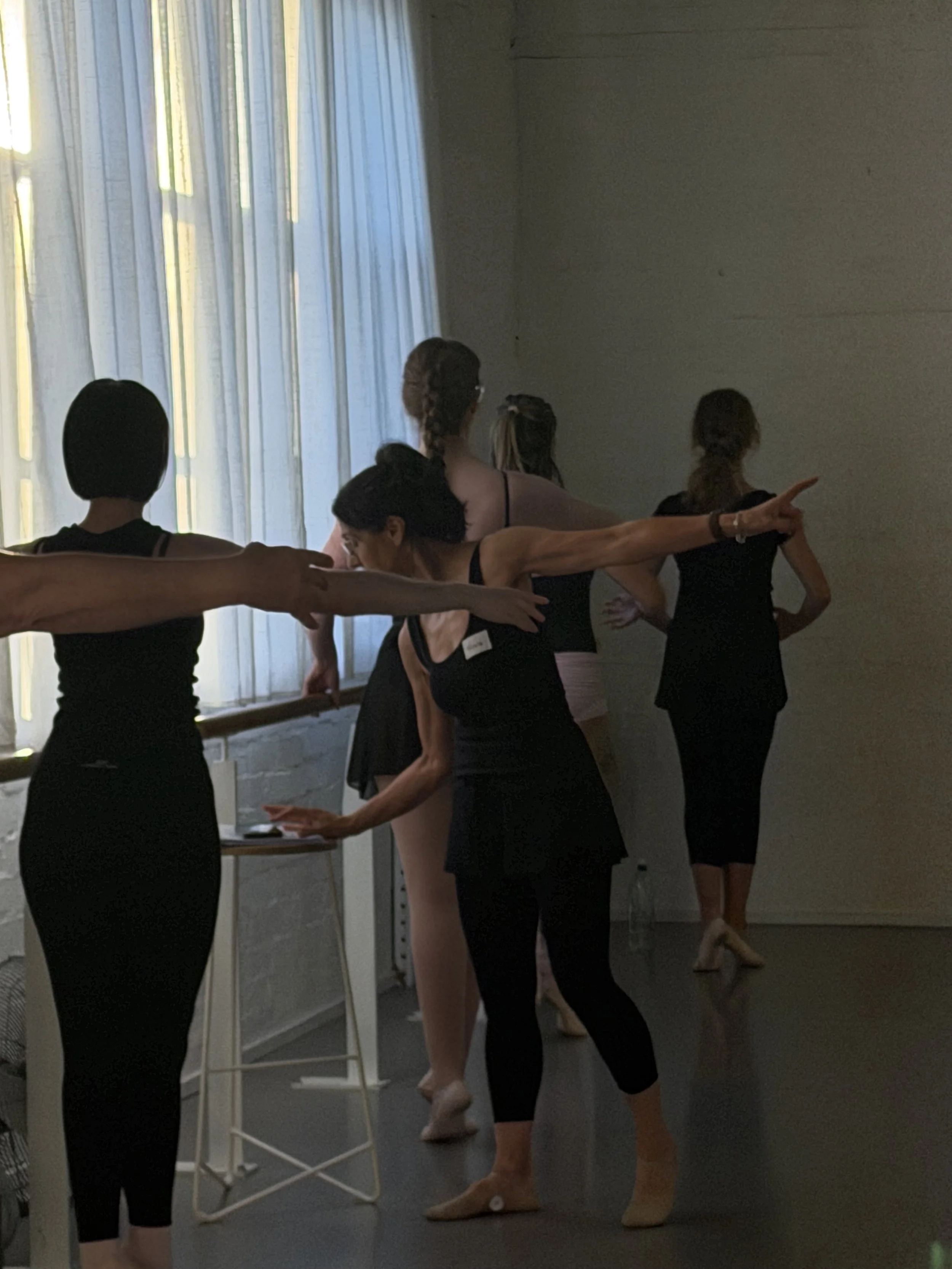 A group of adult ballet dancers practicing in a studio near a window with white curtains at Adult Ballet Centre