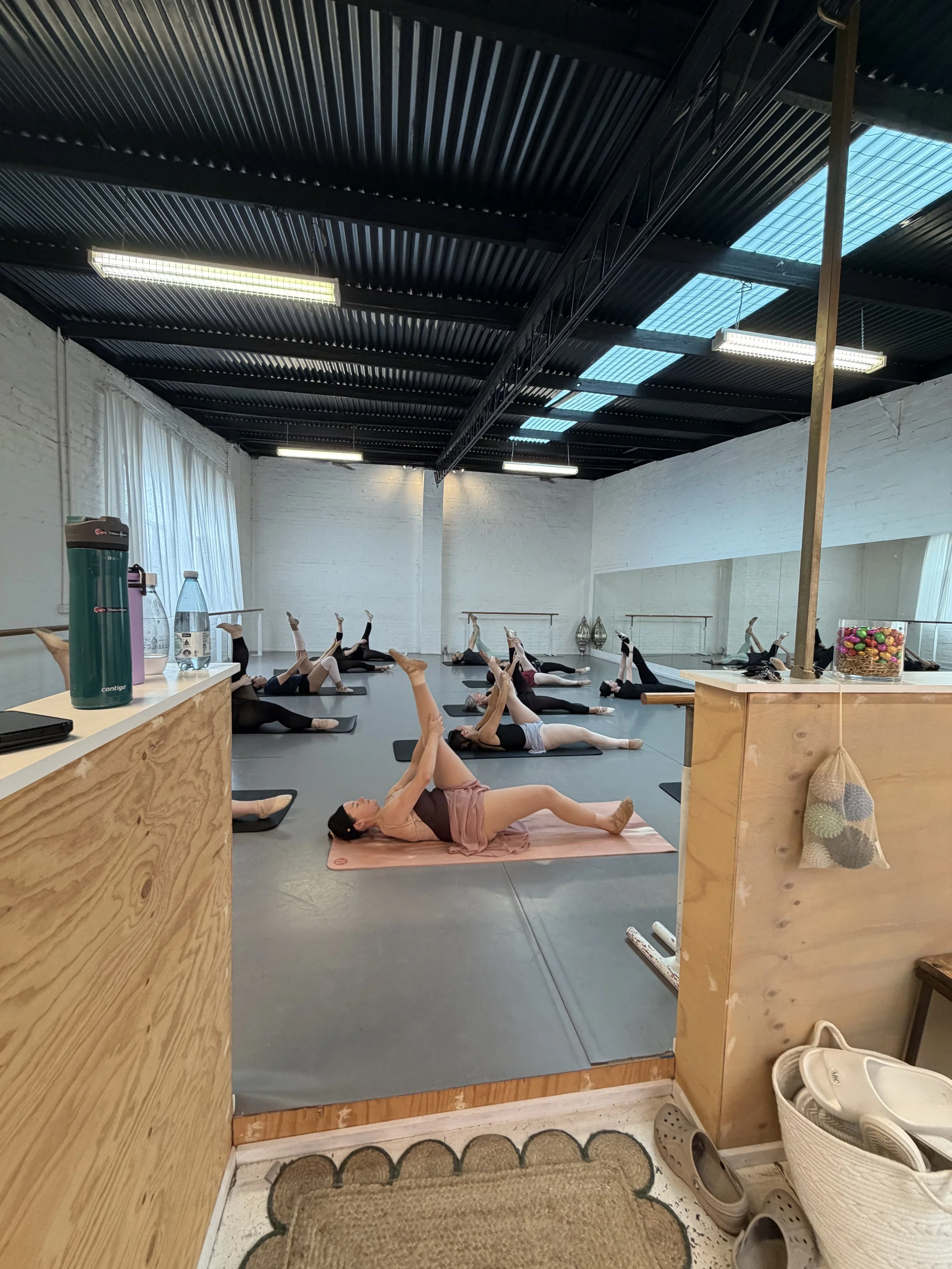 People participating in a yoga or Pilates class in a studio, lying on mats and doing stretching exercises.