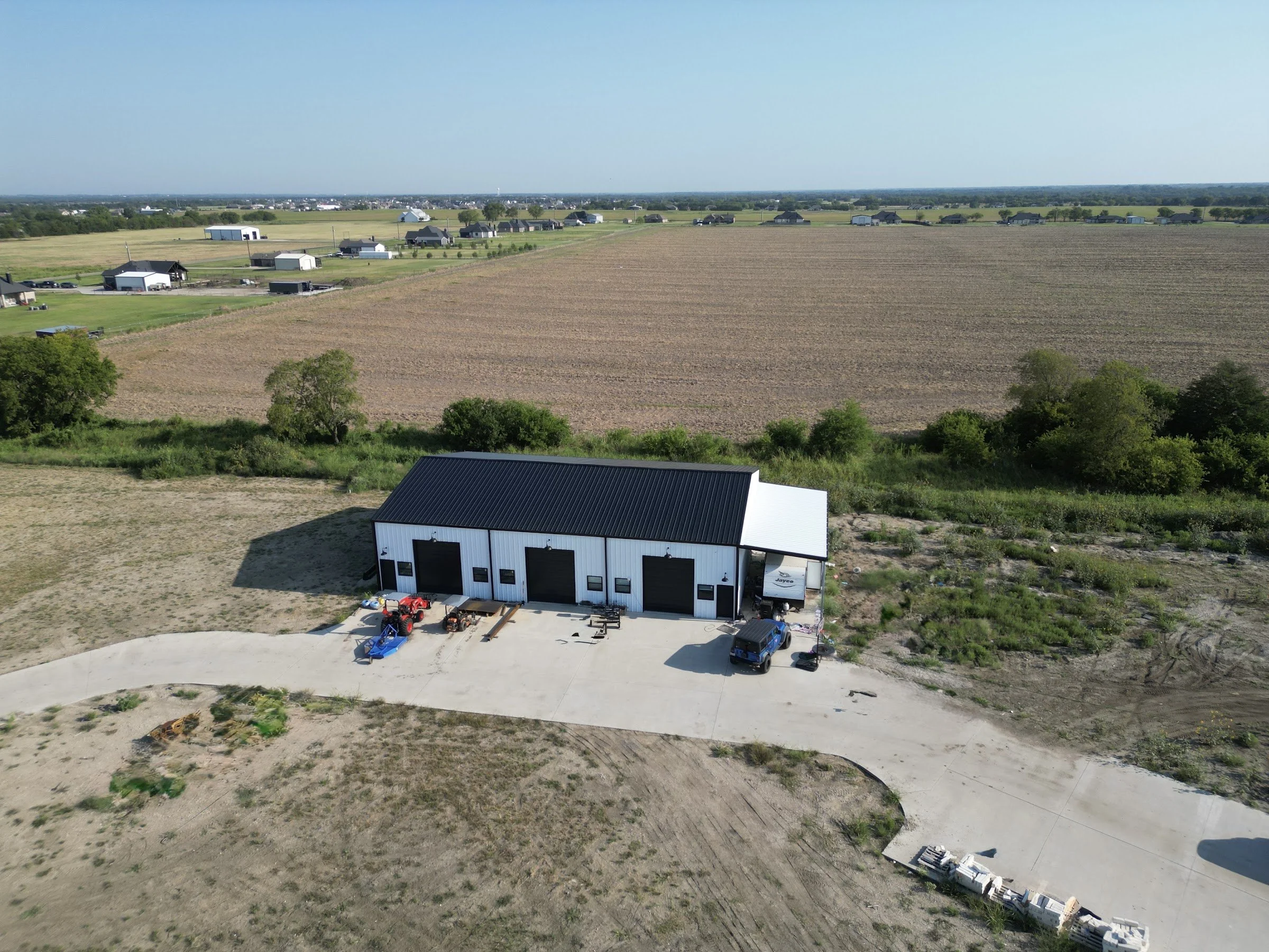 Aerial view of a metal shop on open acreage with concrete drive, showing how site conditions vary from tract to tract
