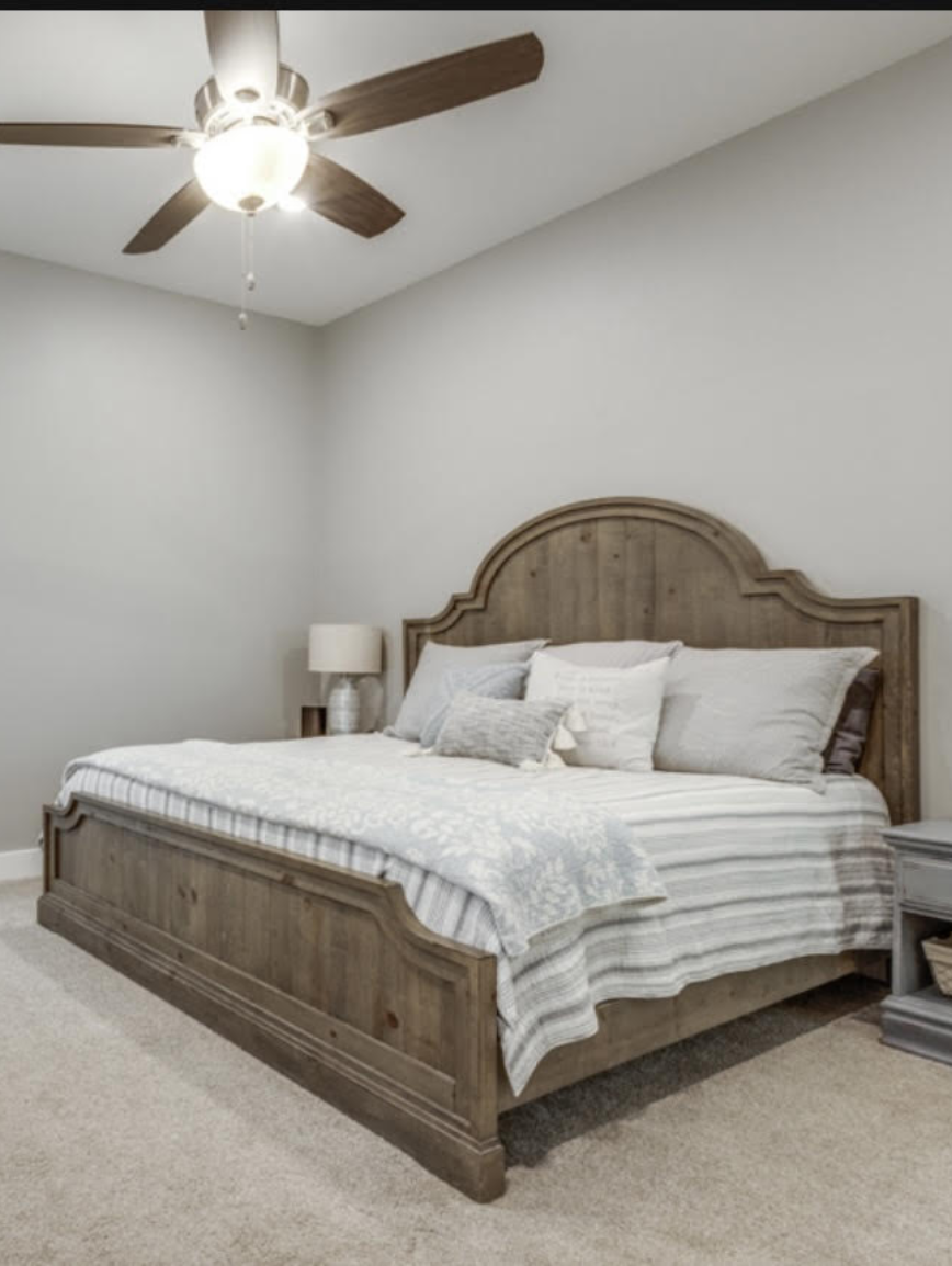 Bedroom with wooden bed, side table, table lamp, and ceiling fan.