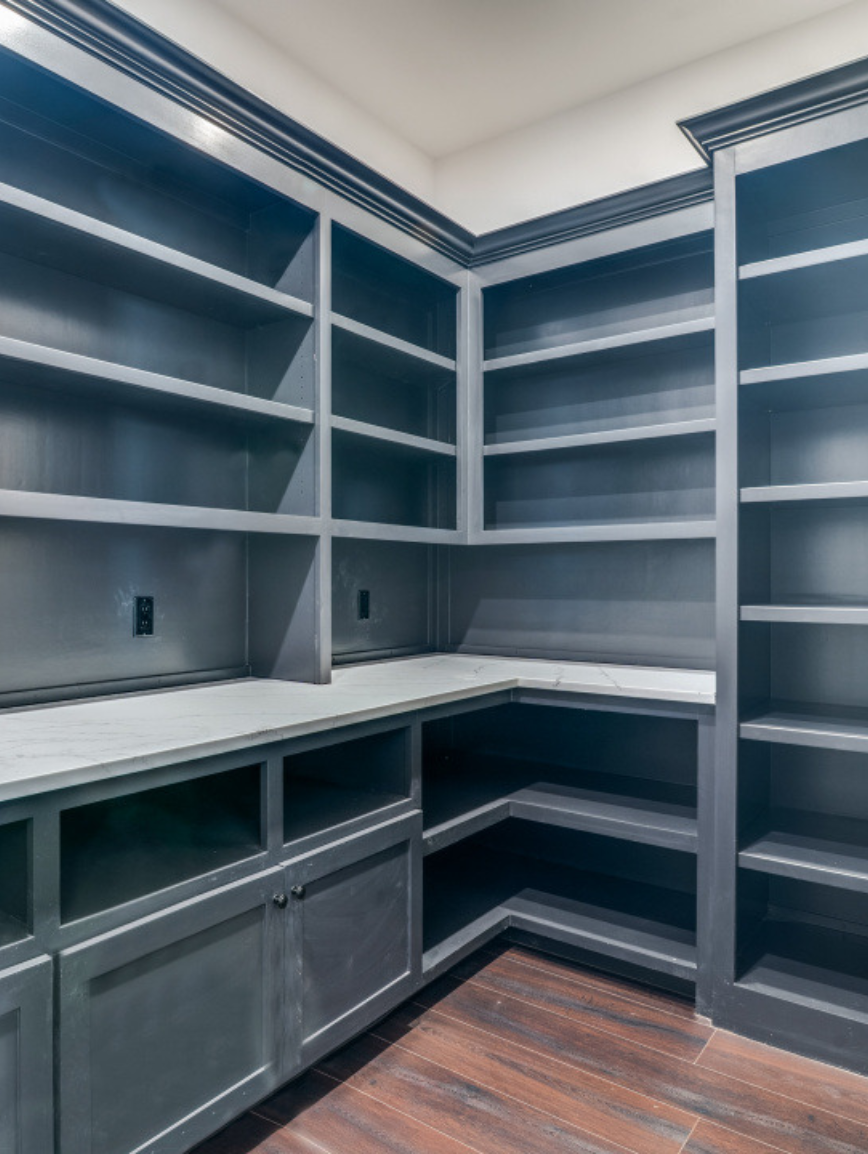 Empty gray built-in shelves and cabinets in a corner kitchen or pantry with wood flooring.