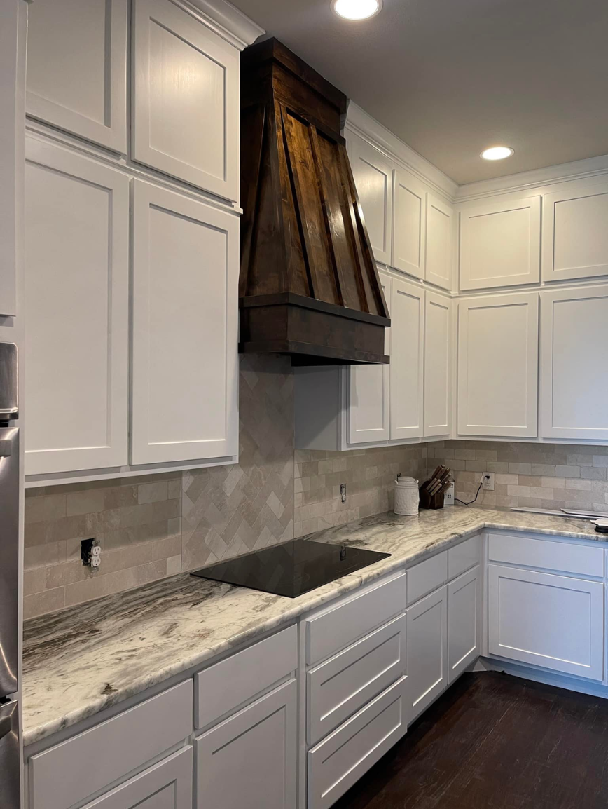Modern kitchen with white cabinets, a granite countertop, and a dark wooden range hood.